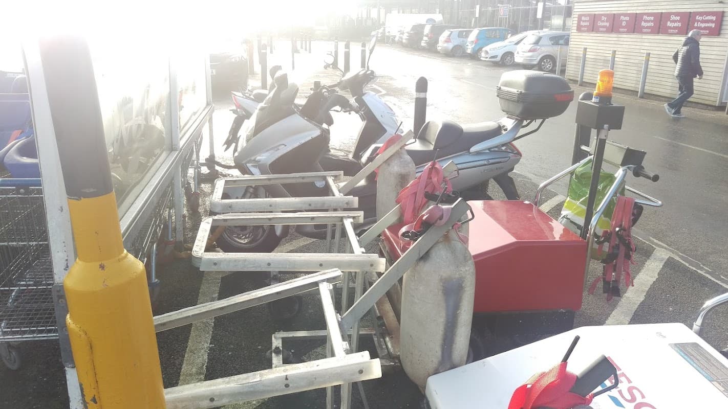 Motorcycles parked in a designated area, with nearby carts and containers, under bright sunlight.