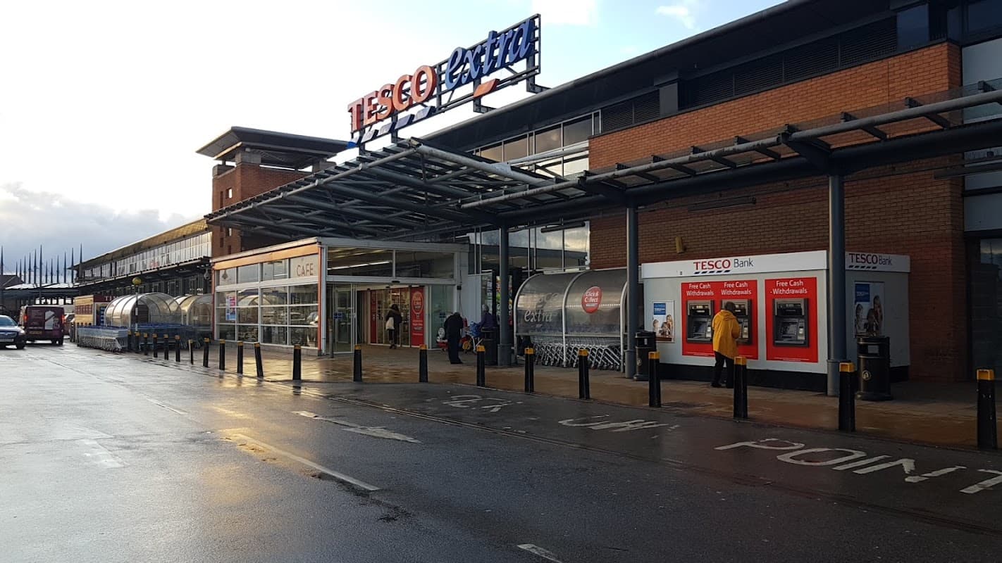 Tesco Express storefront at Seacroft Green Shopping Centre with shoppers and ATMs under a covered walkway.