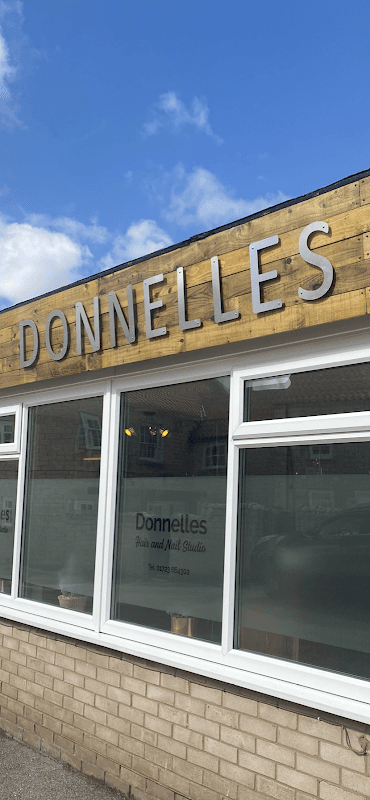 Sign for Donnelles Hair Studio with large letters, windows reflecting a blue sky, and a brick wall below.