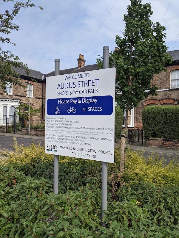 Welcome sign for Audus Street Short Stay Car Park, detailing payment and parking information, surrounded by greenery.