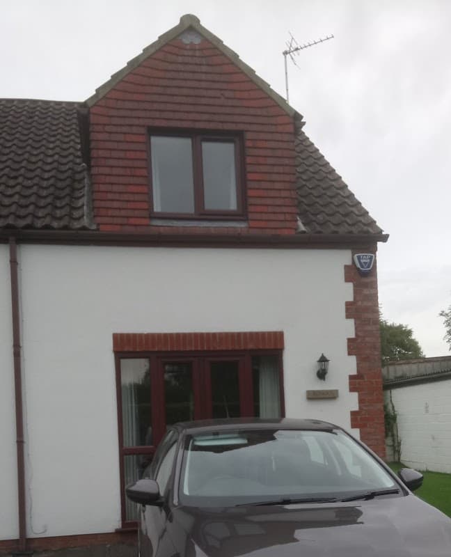 Charming cottage with a red-brick facade, sloped roof, and a parked car in front, set in a rural area.