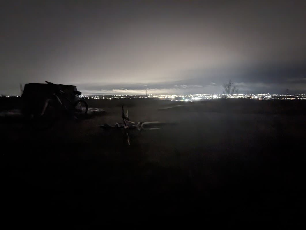 Dimly lit car park at night with a distant view of city lights and a bicycle on the ground.