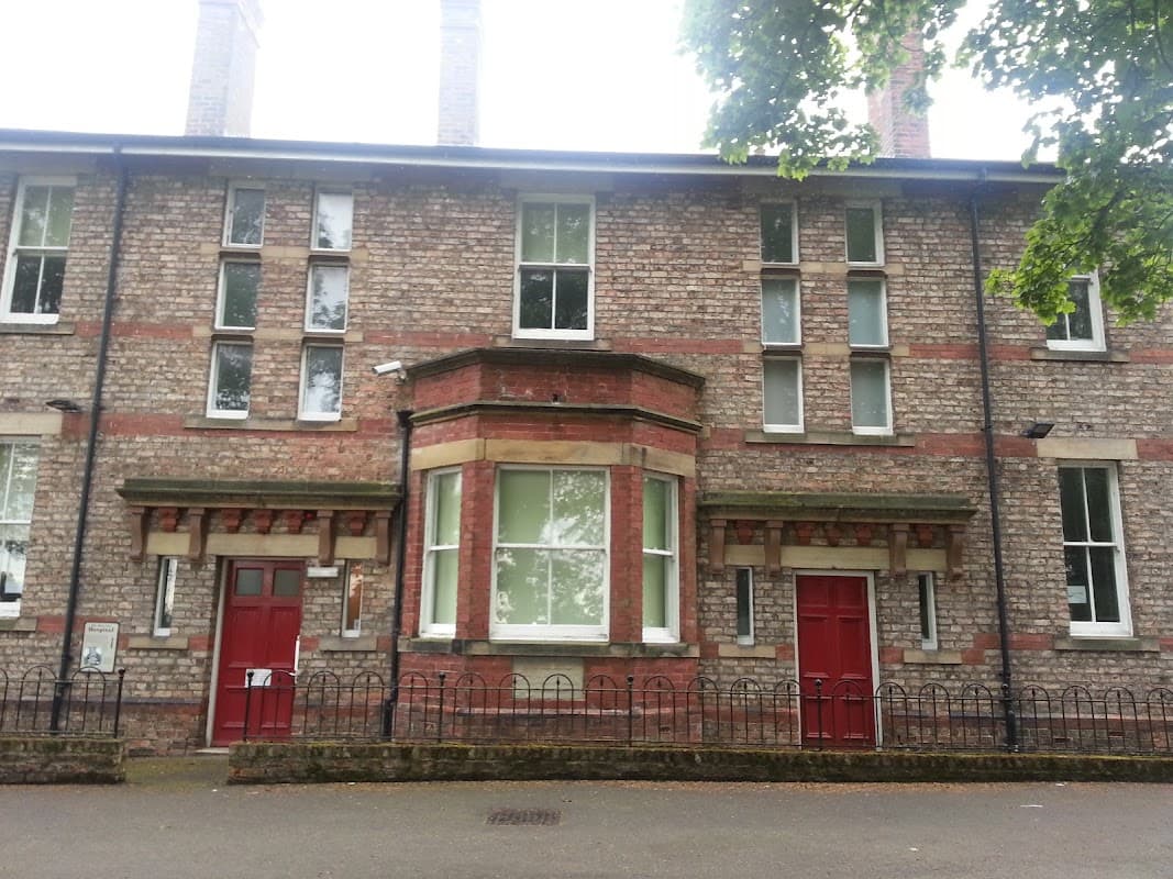 Victorian-style brick building with red doors, large windows, and a decorative entrance in a tree-lined setting.