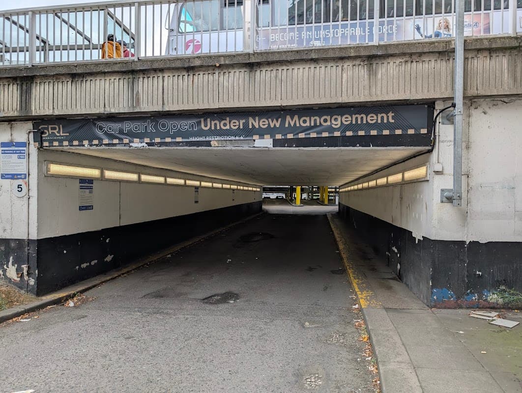 Multi-storey car park entrance with "Car Park Open Under New Management" sign and dimly lit tunnel.