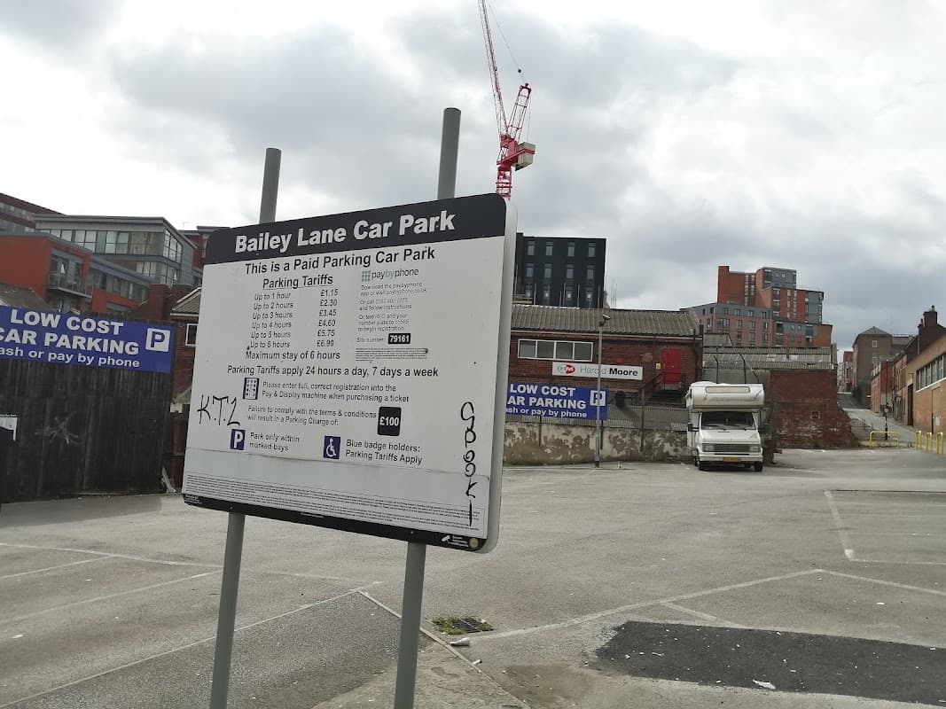 Bailey Lane Car Park sign with parking tariffs, empty lot, and buildings in the background under a cloudy sky.