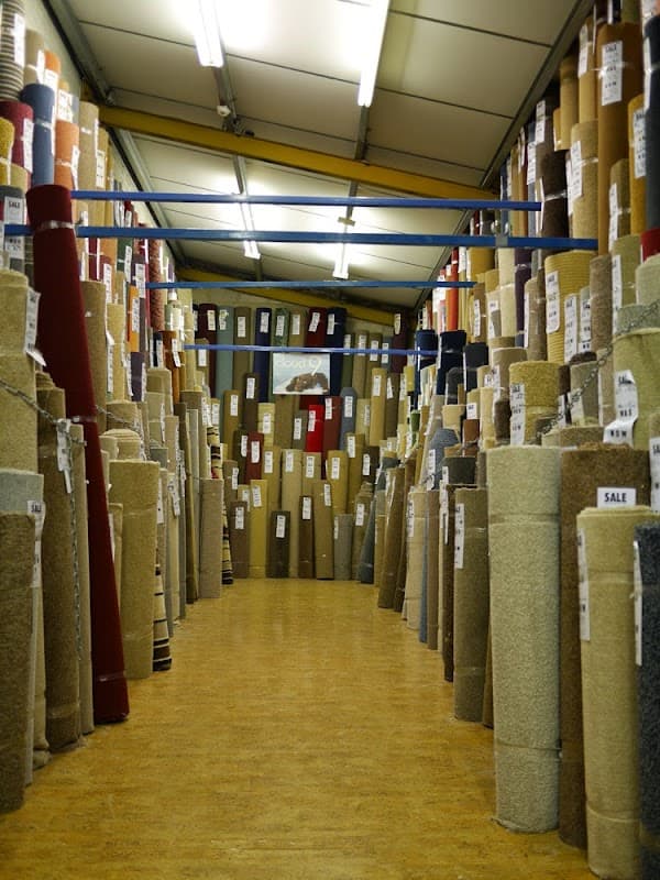 A wide aisle lined with rolls of carpets in various colors and textures, labeled for sale in a carpet store.