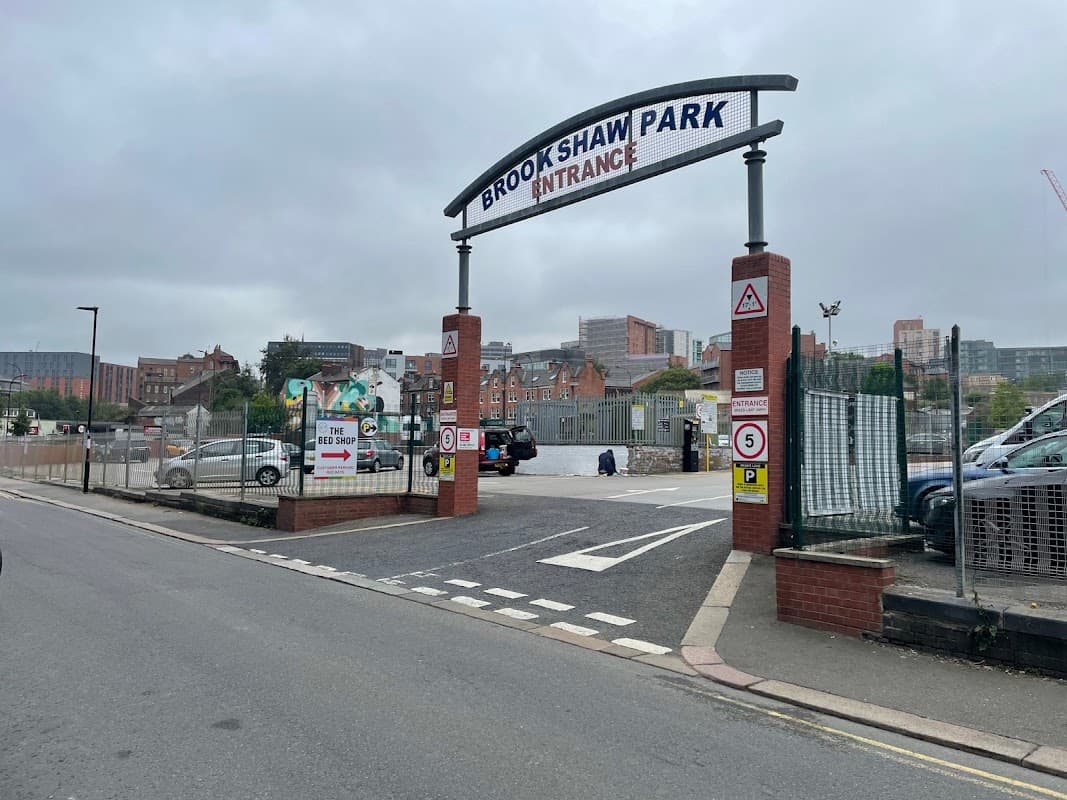 Entrance to Brookshaw Park Car Park with signage, barriers, and surrounding buildings in Sheffield, Yorkshire.