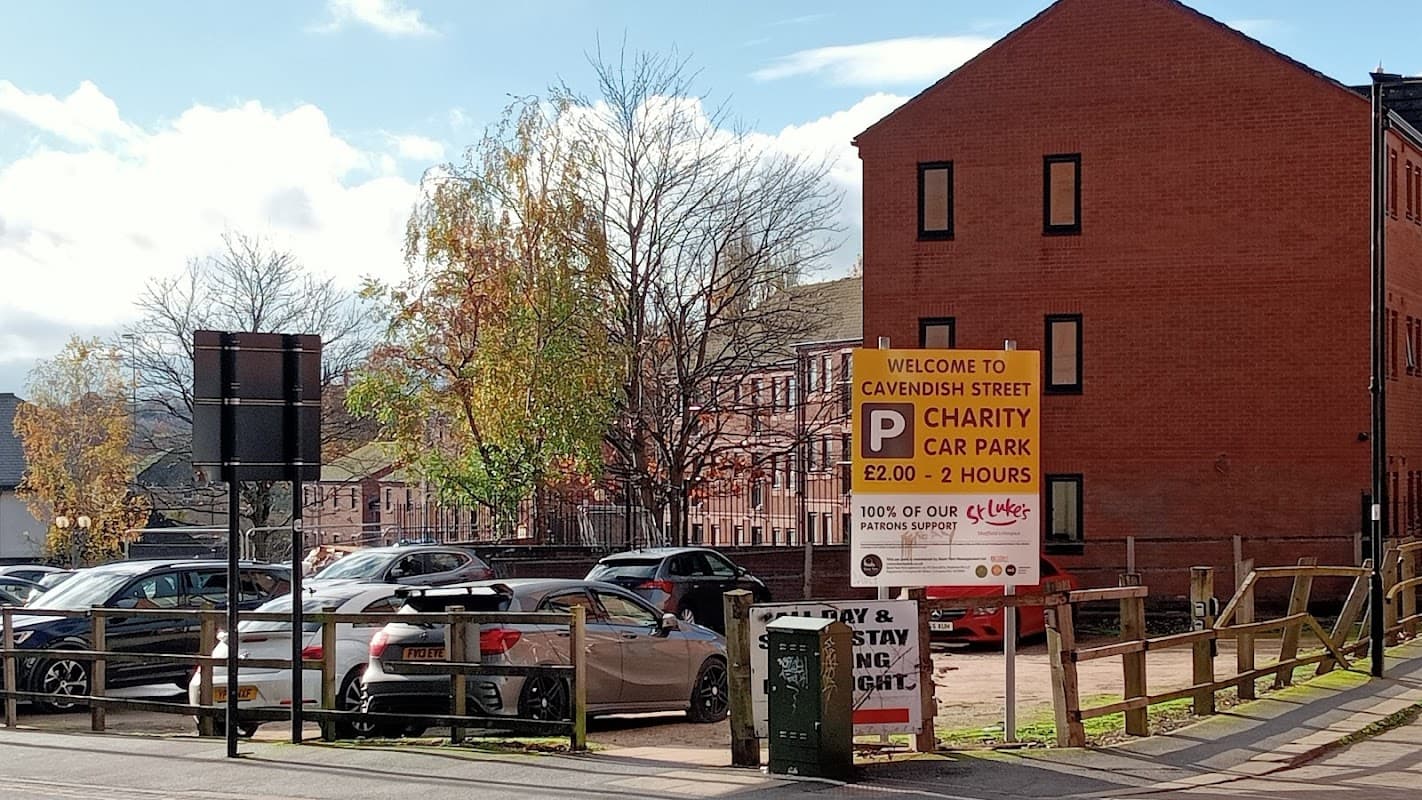 Cavendish Street Car Park sign with pricing, parked cars, and nearby red brick buildings under a clear blue sky.