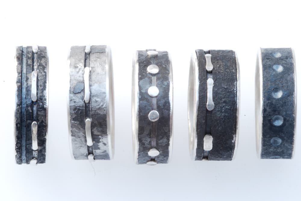 Five unique metal rings with textured surfaces and varying designs, displayed against a white background.