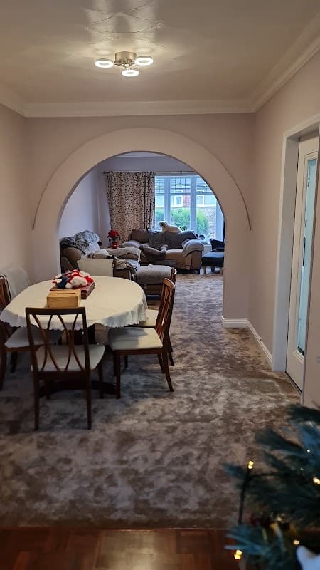 Dining area with a round table and chairs, leading to a cozy living room with a sofa and large windows.