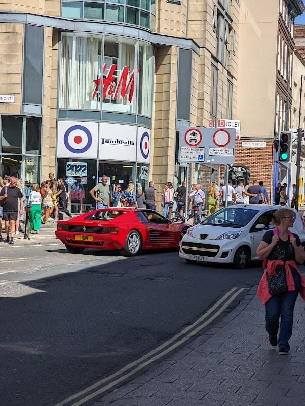 H&M store with a crowd outside, featuring a red sports car and a white compact car on a busy Sheffield street.