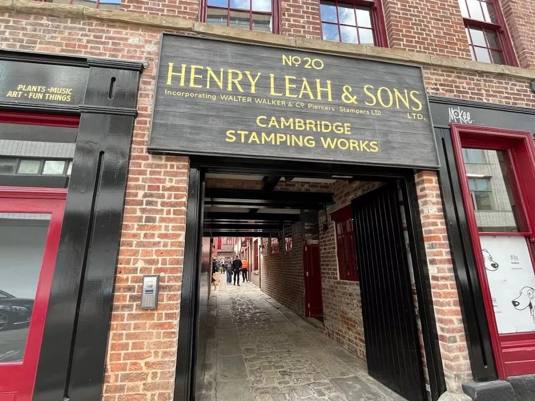 Brick archway entrance with a wooden sign for "Henry Leah & Sons" and people walking through Leah's Yard in Sheffield.