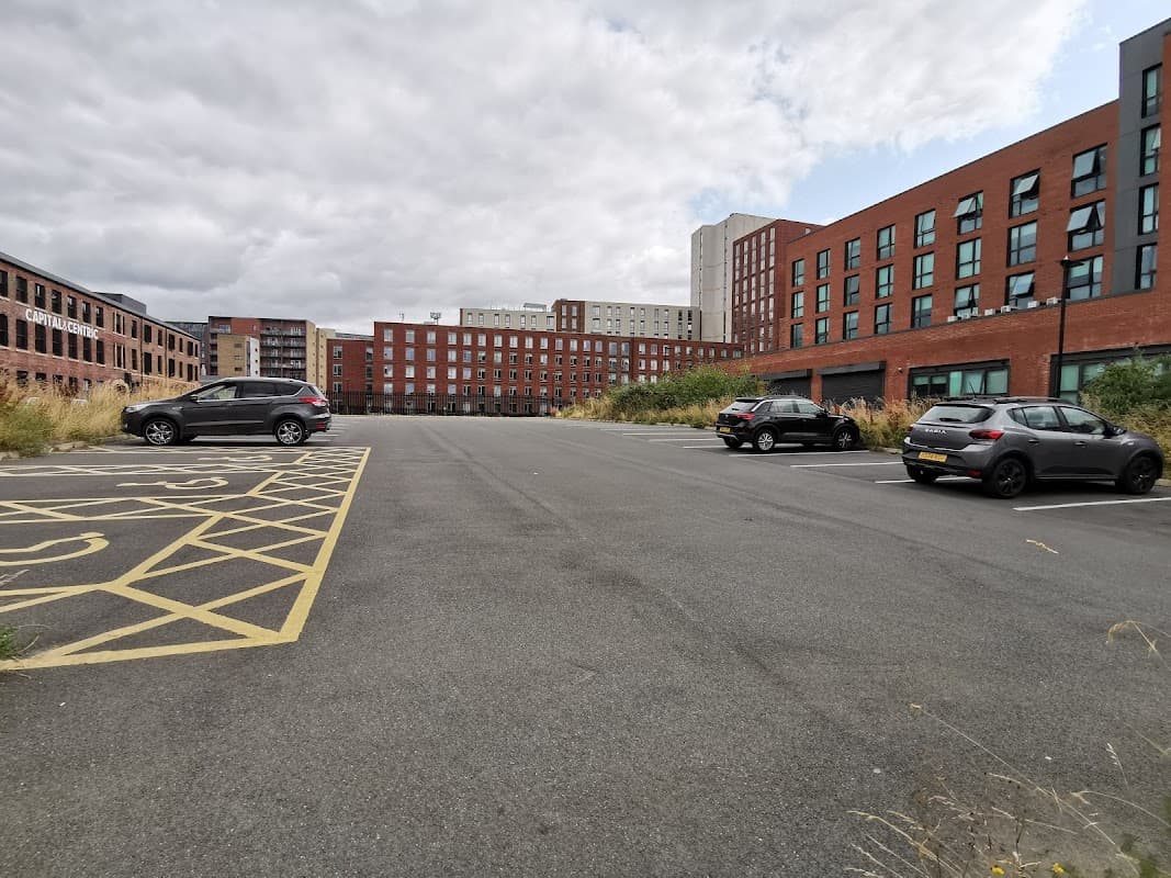 Milton Street Car Park with empty spaces, surrounded by modern brick buildings under a cloudy sky.