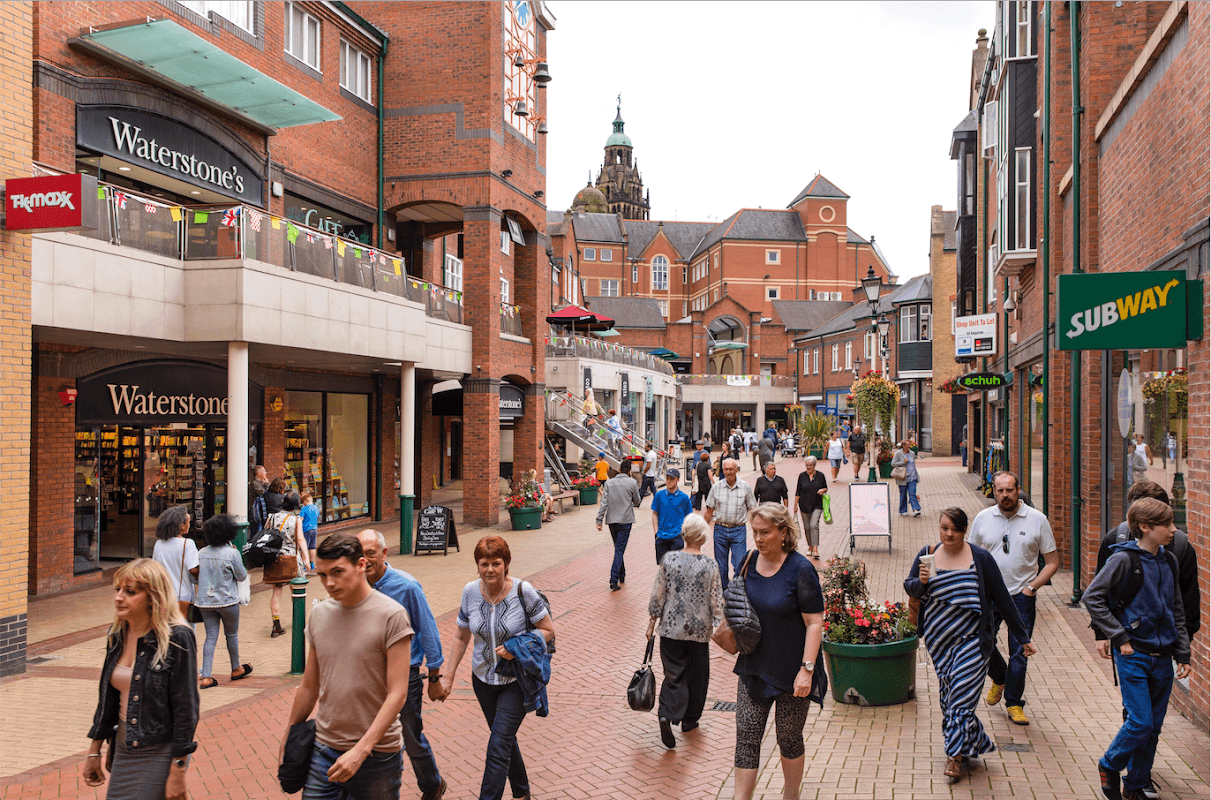 Busy shopping street in Orchard Square, Sheffield, featuring stores like Waterstone's and Subway, with people walking.