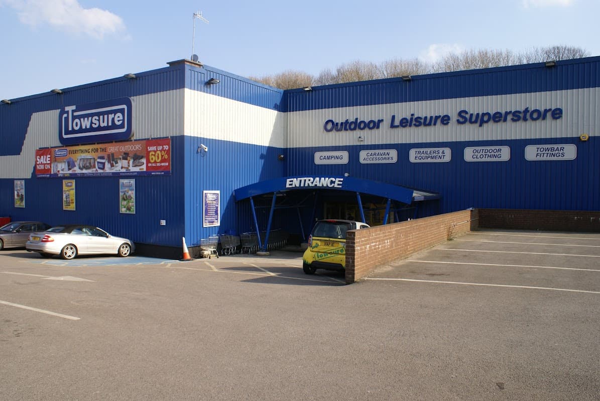 Blue building with "Towsure" sign, parking lot, and entrance; features outdoor leisure products and sales signage.