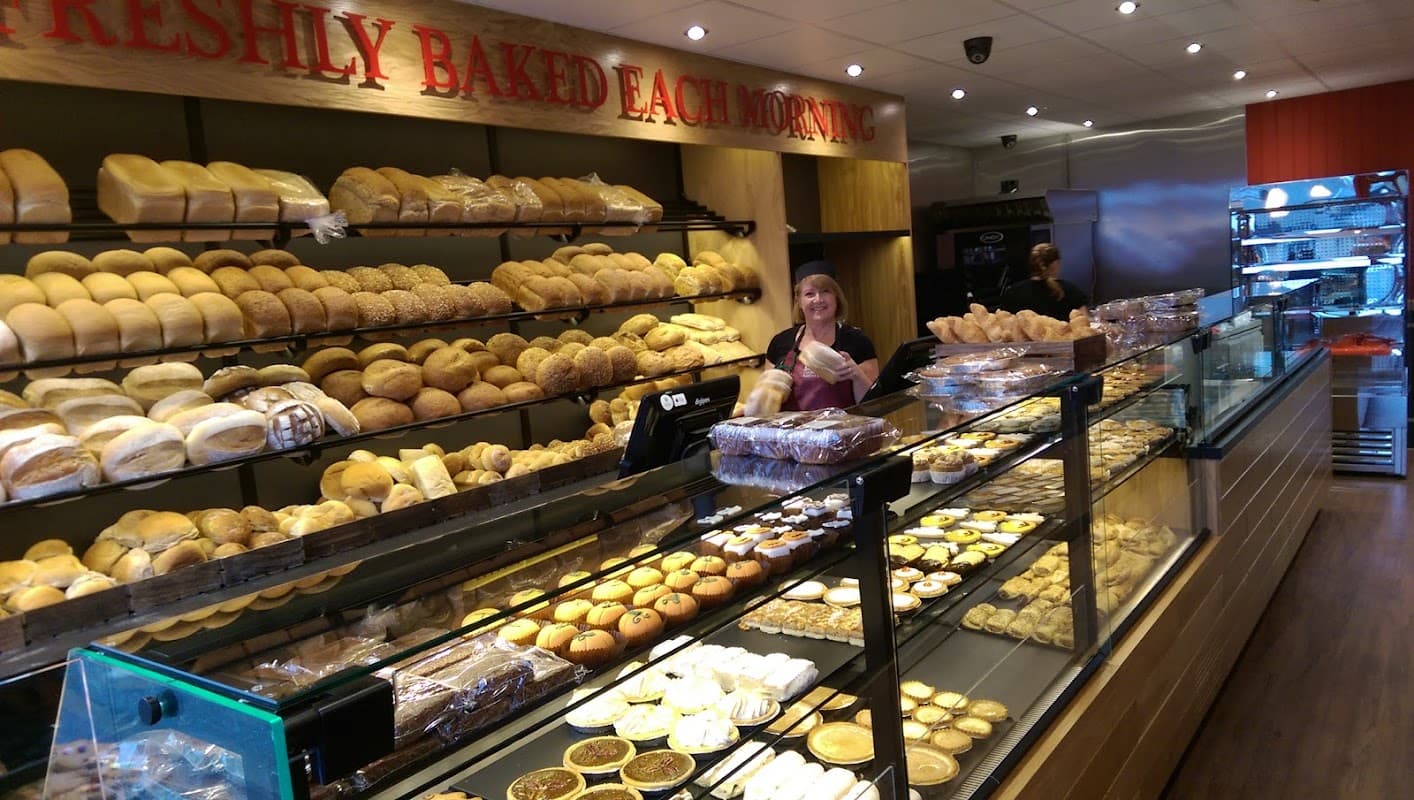 A bakery display filled with various bread rolls, pastries, and a smiling staff member behind the counter.