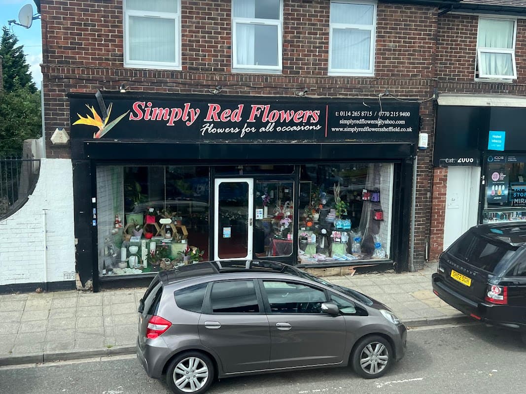 Florist shop front with "Simply Red Flowers" sign, displaying flowers and gifts in the window, parked cars nearby.