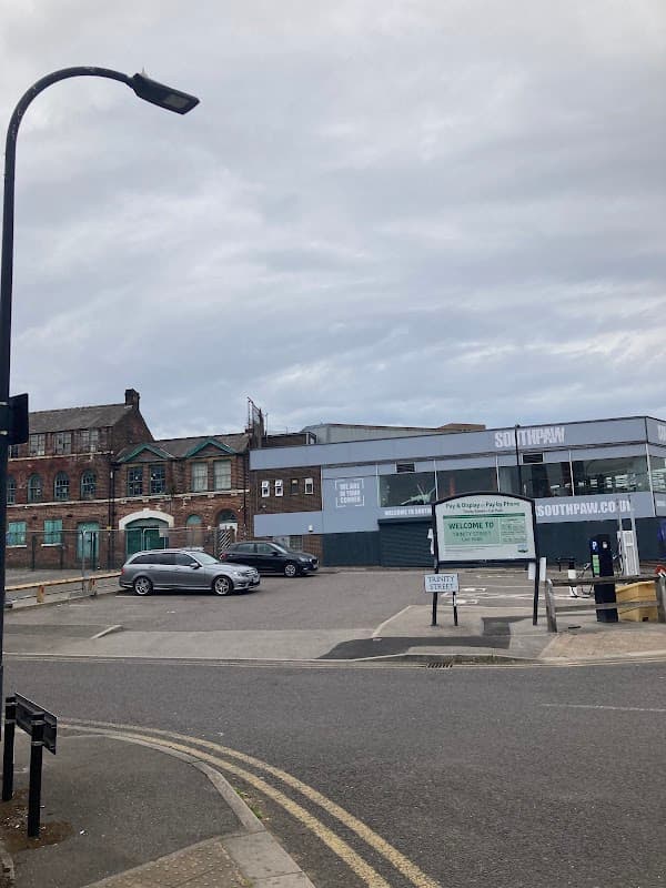 Trinity Street Car Park with parked cars, a sign reading "WELCOME TO SOUTHPAW," and industrial buildings in the background.