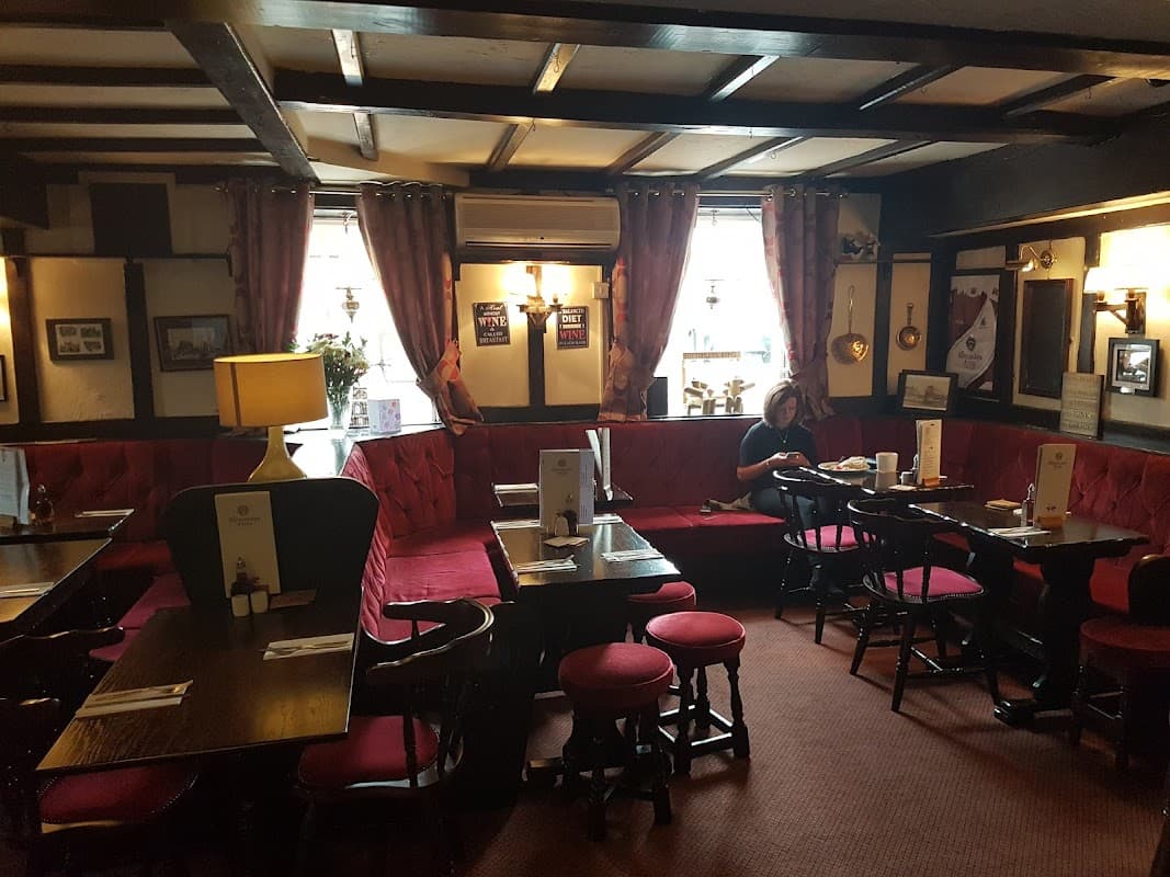 Cozy restaurant interior with red upholstered seating, wooden tables, and warm lighting, featuring a woman at a table.