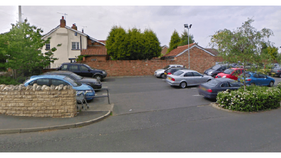 Pay & Display parking area in Sherburn in Elmet, with cars parked and greenery surrounding a stone wall.