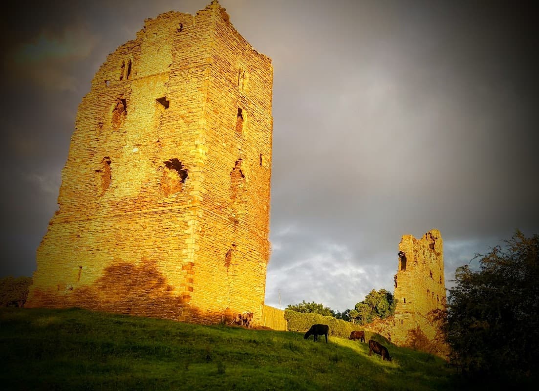 Historic stone ruins on a grassy hill, with grazing cows and a dramatic sky in Sheriff Hutton, Yorkshire.