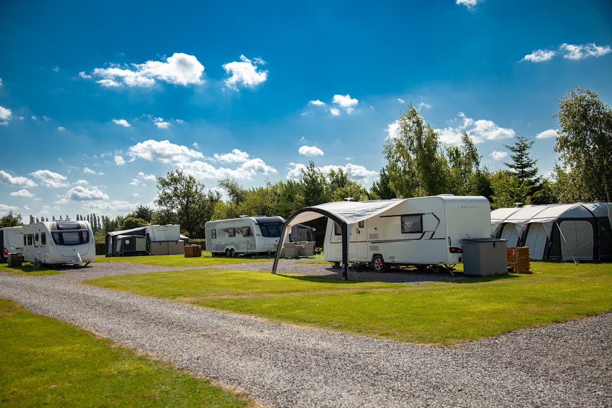 Caravans and tents set on a grassy area under a bright blue sky with scattered clouds at York Meadows Caravan Park.