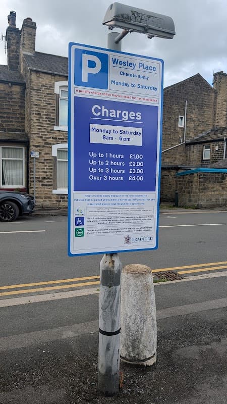 Signpost displaying parking charges and operating hours for Wesley Place Car Park in Silsden, Yorkshire.