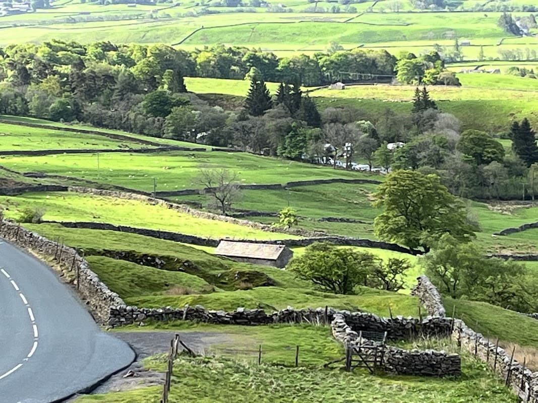 Scenic view of lush green hills, stone walls, and a winding road near Shaw Ghyll Caravan and Camping in North Yorkshire.
