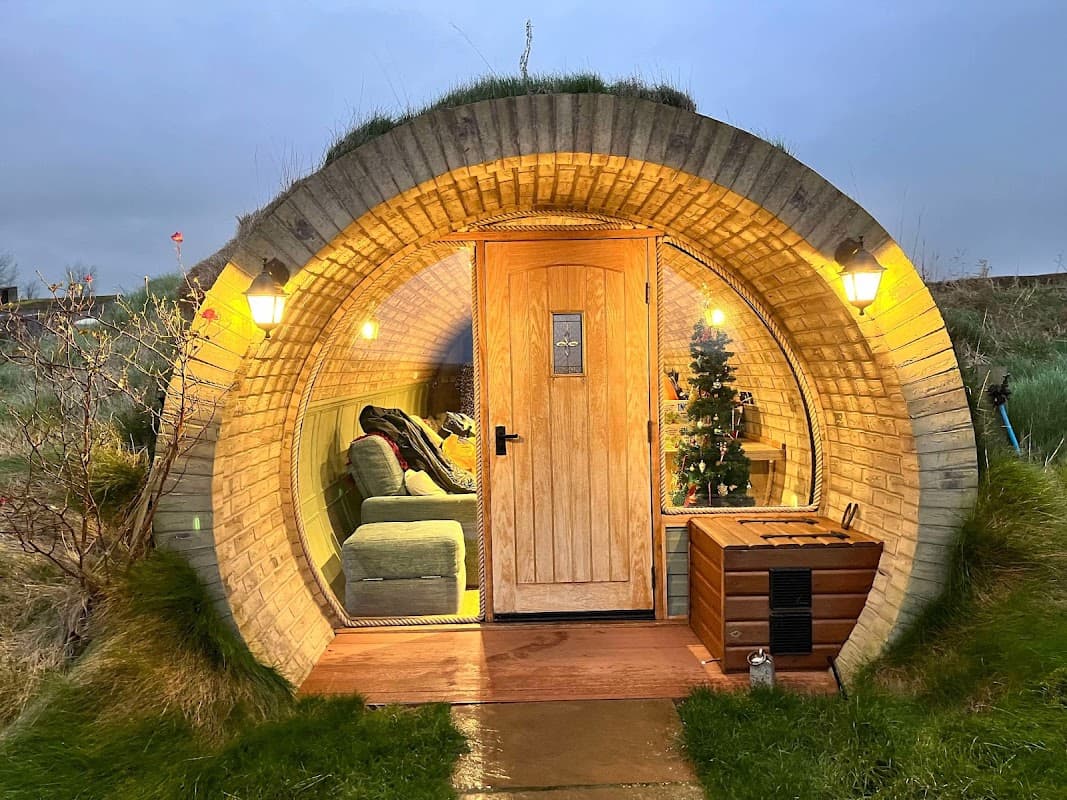 Cozy round cabin with a wooden door, soft seating, and decorative lights, surrounded by grassy landscape.