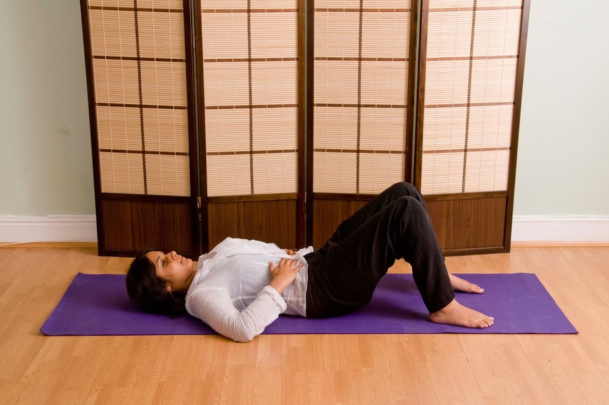 A woman lies on a yoga mat in front of a wooden screen, practicing the Alexander Technique in a calm setting.