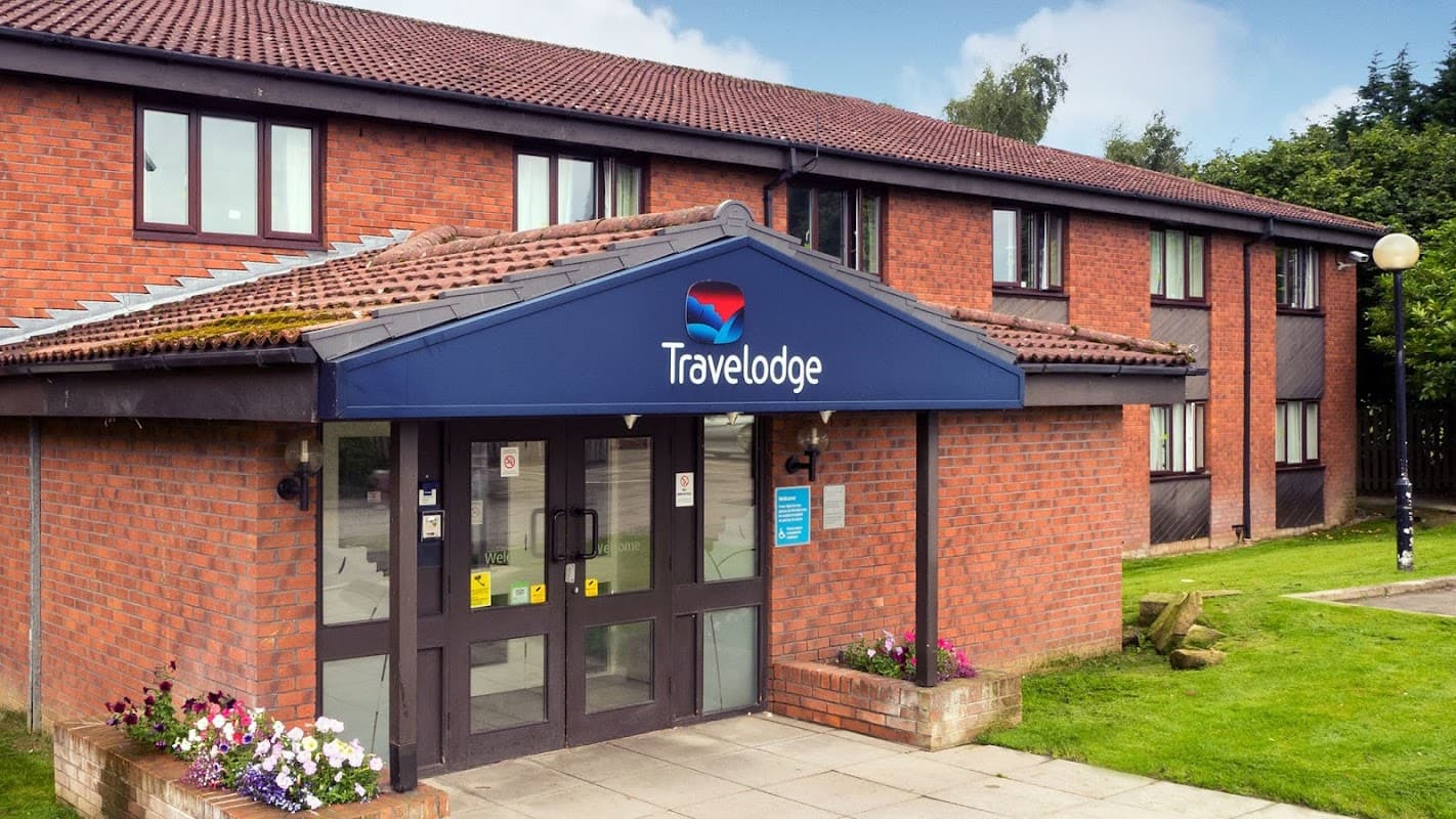 Travelodge building with a blue entrance canopy, brick facade, and colorful flower beds in Skeeby, Yorkshire.