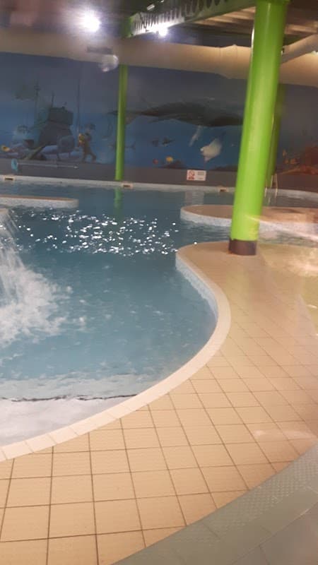 Indoor swimming pool with a splash area, surrounded by colorful murals and green pillars.