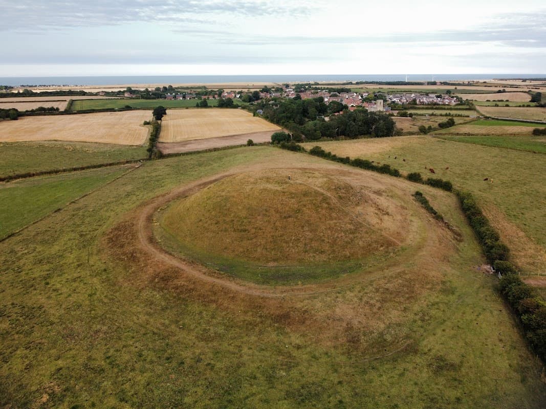 Aerial view of Skipsea Castle mound surrounded by fields and distant coastal landscape in Yorkshire.