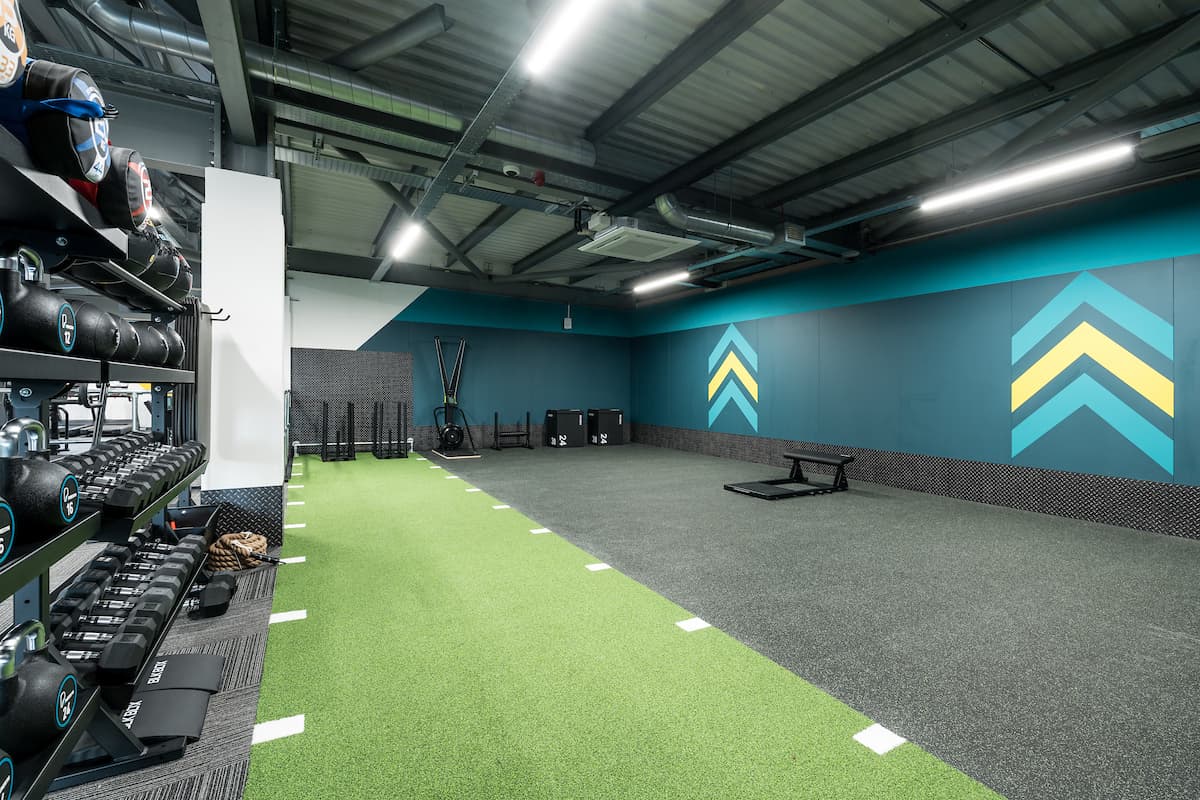 Modern gym interior with turf flooring, weights, and workout equipment against vibrant teal and yellow walls.