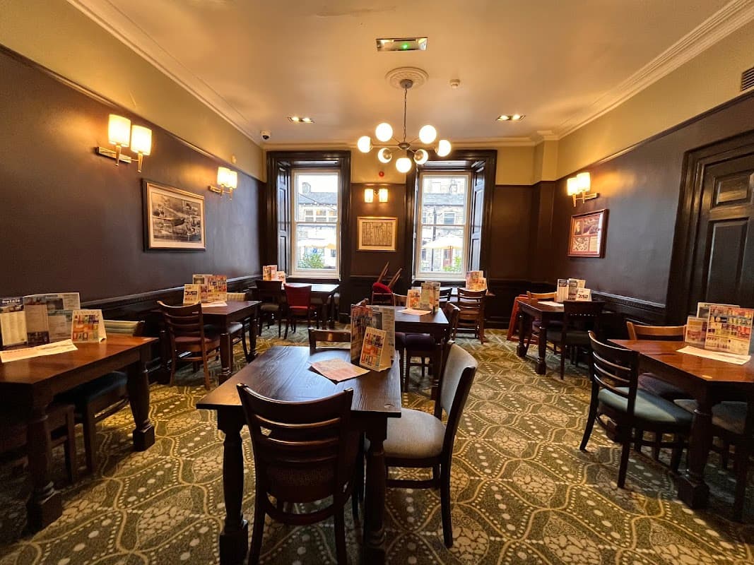 Cozy restaurant interior with wooden tables, chairs, and patterned carpet, featuring large windows and warm lighting.