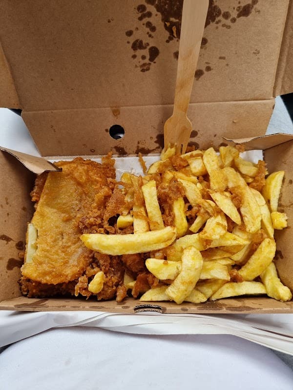 Golden-brown fish fillet with crispy batter alongside a generous serving of golden fries in a takeaway box.