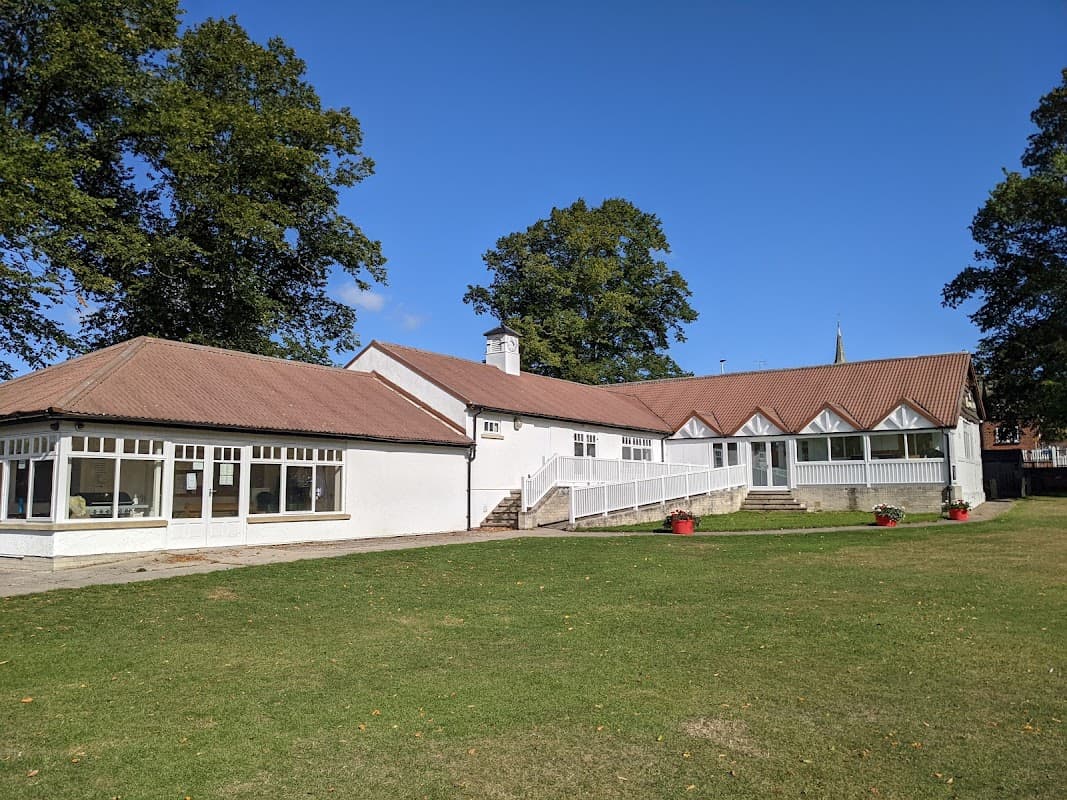 Snainton Village Hall features a white exterior, large windows, a sloping roof, and a green lawn surrounded by trees.