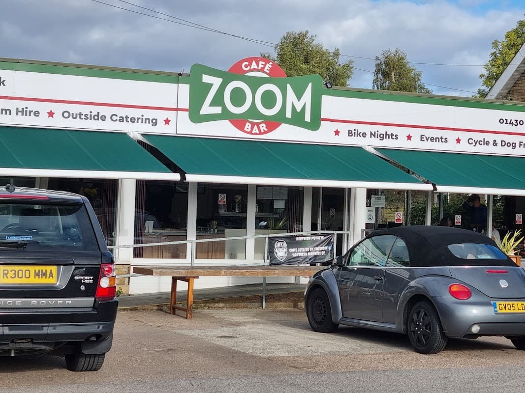 Zoom Cafe Bar features a green awning, outdoor seating, and parked cars in front of a welcoming storefront.