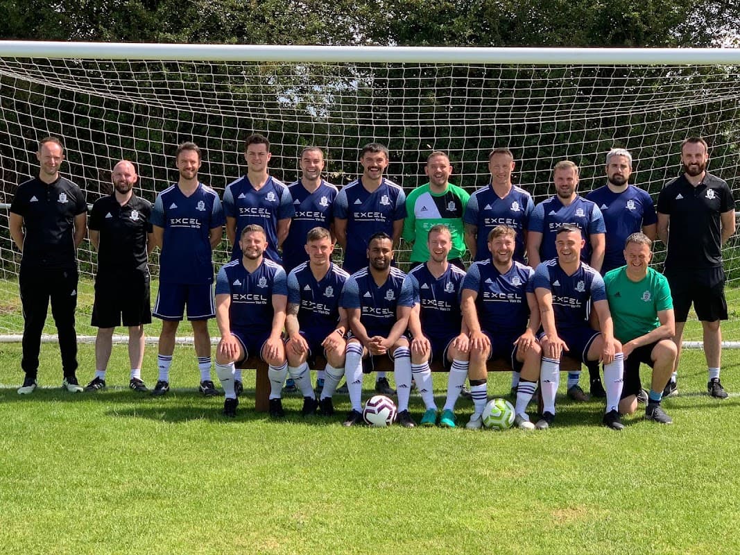 South Milford Football Club team poses in blue jerseys on a grassy field with a goal net in the background.