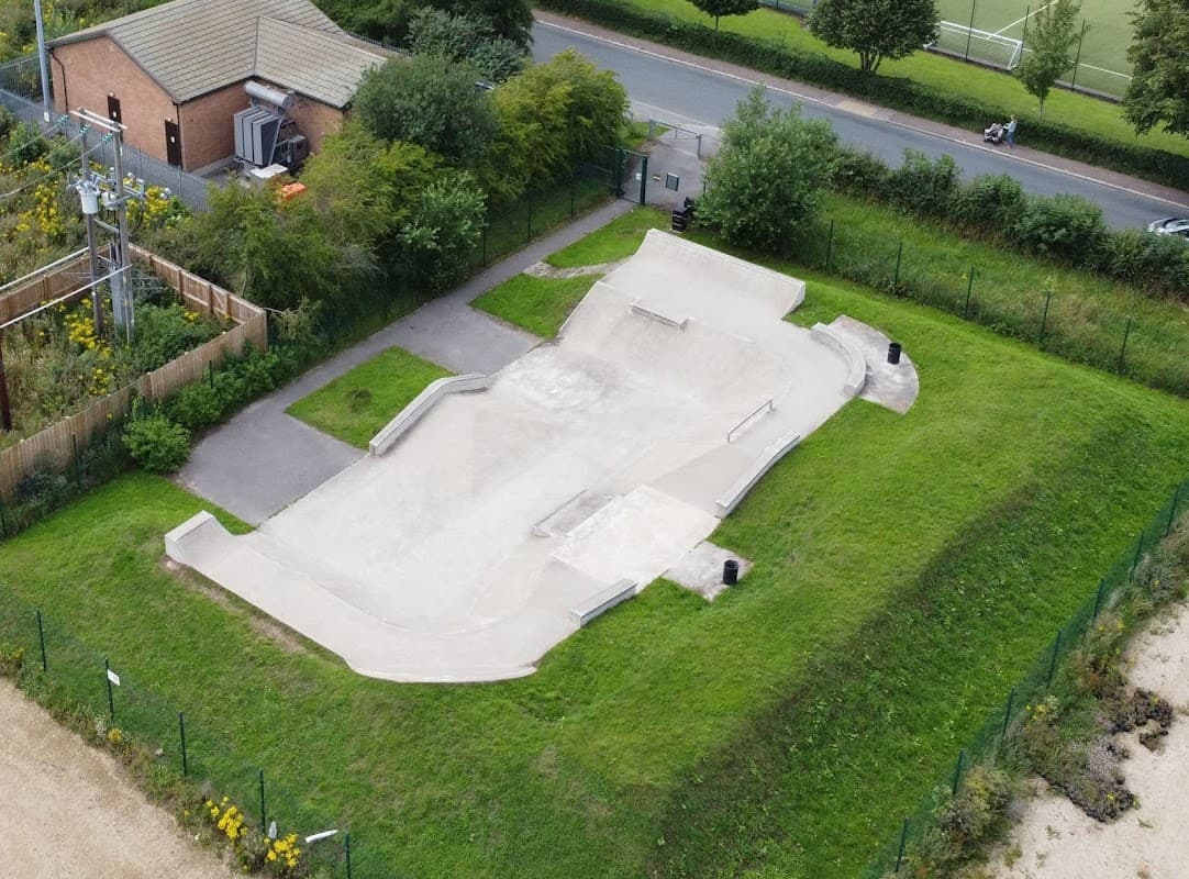 Aerial view of Thirsk Skatepark featuring concrete ramps, green grass, and nearby trees along a road.