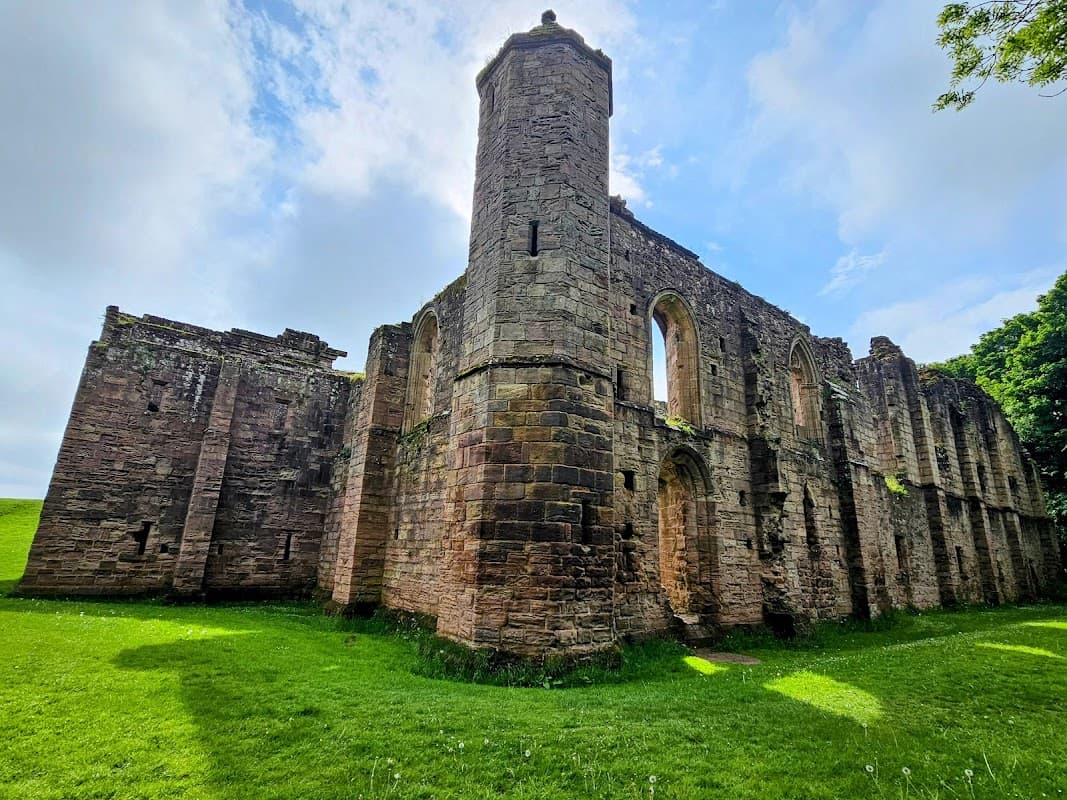 Ruins of Spofforth Castle featuring stone walls, arched windows, and a tower, surrounded by lush green grass.