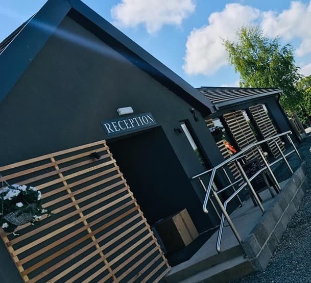 Modern bar venue with wooden slatted exterior, sign reading "RECEPTION," and a clear blue sky above.