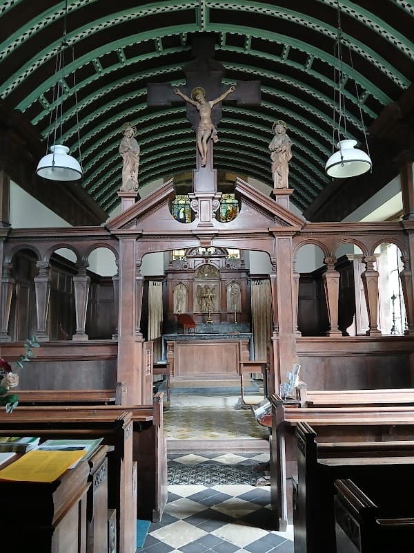 Interior of St Chad's Church featuring wooden pews, a crucifix, and stained glass above the altar.