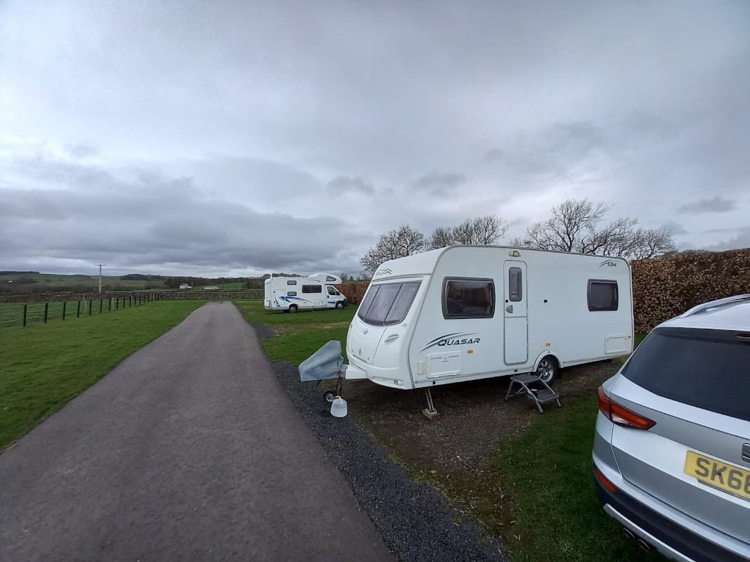 Caravans parked along a gravel path, with green fields and cloudy skies in the background at Brigholme Farm.