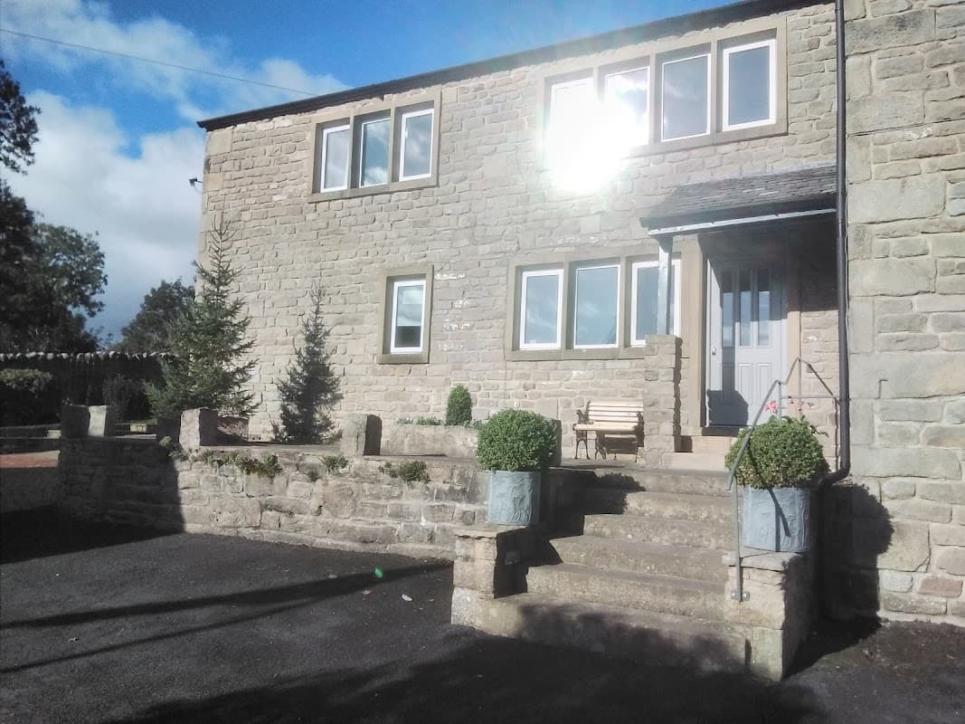 Stone exterior of Valleymead Guest House with steps, potted plants, and a wooden bench under a sunny sky.