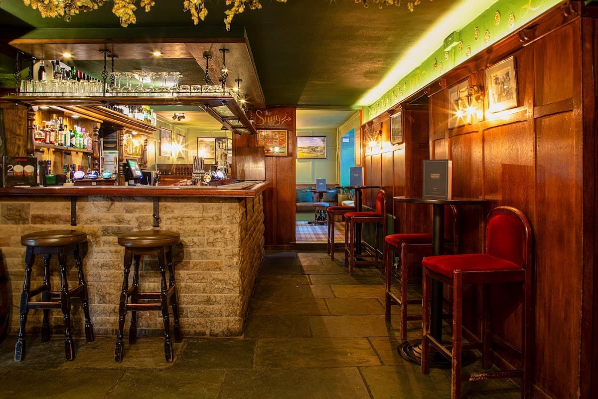 Warm wooden interior with a bar, stools, and dim lighting, creating a cozy atmosphere in Craven Heifer, Stainforth.