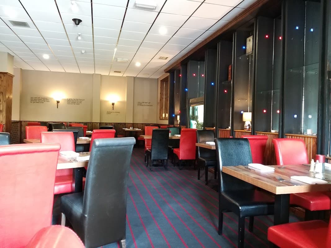 Interior of The Old Poste House Restaurant featuring red and black seating, wooden tables, and ambient lighting.