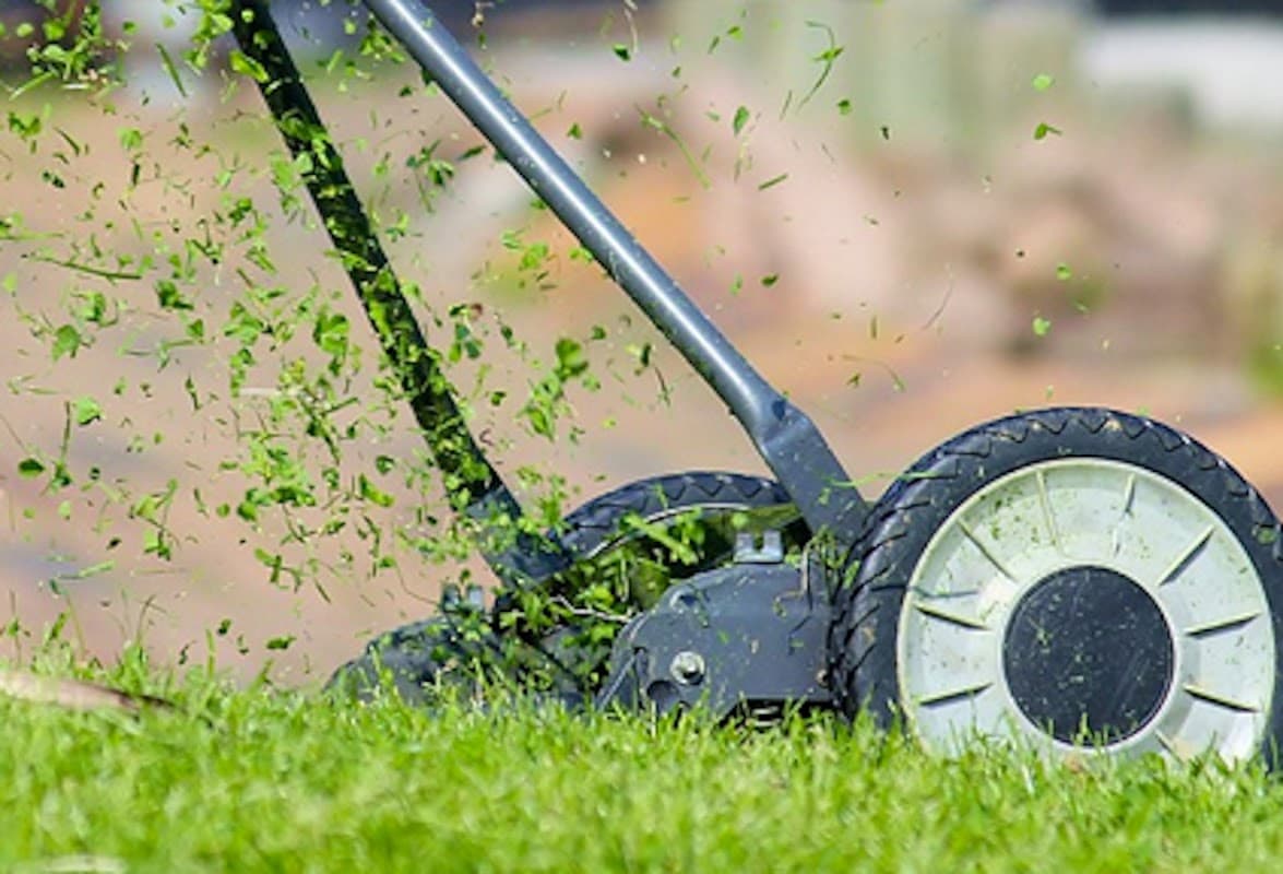 Lawnmower cutting grass, with clippings flying in the air, set against a green lawn background.
