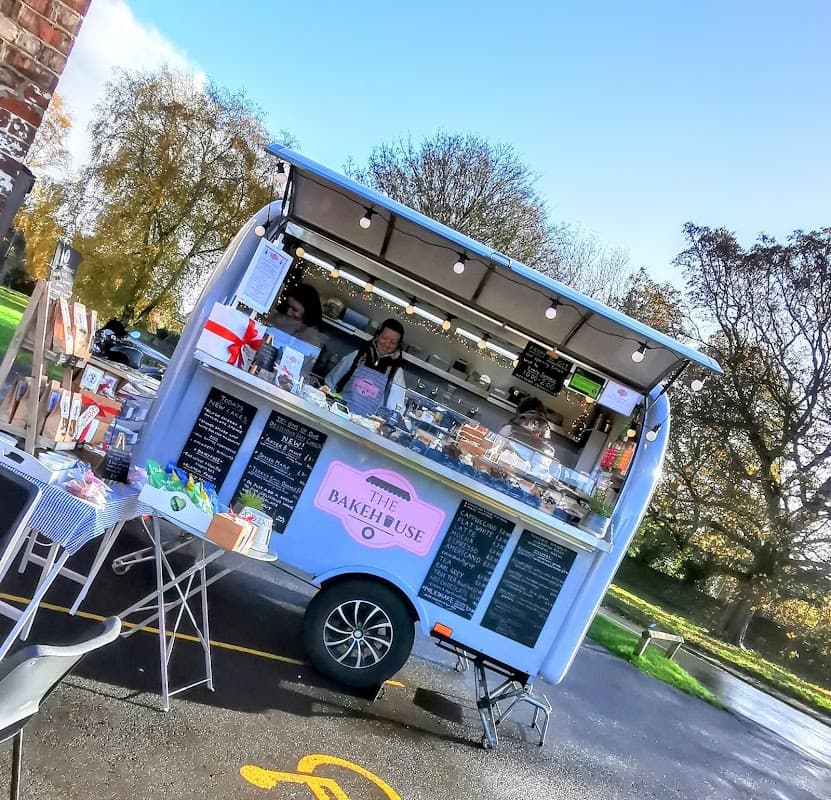 A vibrant food truck with "The Bakehouse" sign serving baked goods, surrounded by trees and clear blue skies.