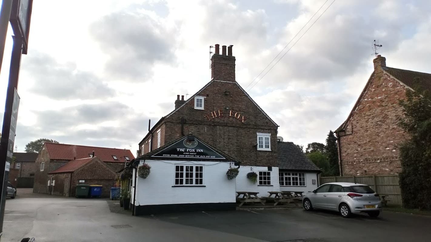 Charming brick guest house with outdoor seating, surrounded by greenery and traditional Yorkshire architecture.